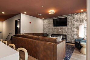 A modern living room with a brown leather sofa, a flat-screen TV mounted on the wall, and a patterned wallpaper. - Two-Bedroom Suite - Unit 201 (Nashville)