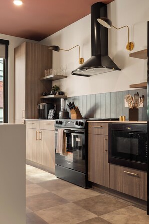 Una cocina moderna con horno empotrado, estufa y microondas. Cuenta con gabinetes de madera y una encimera con fregadero.