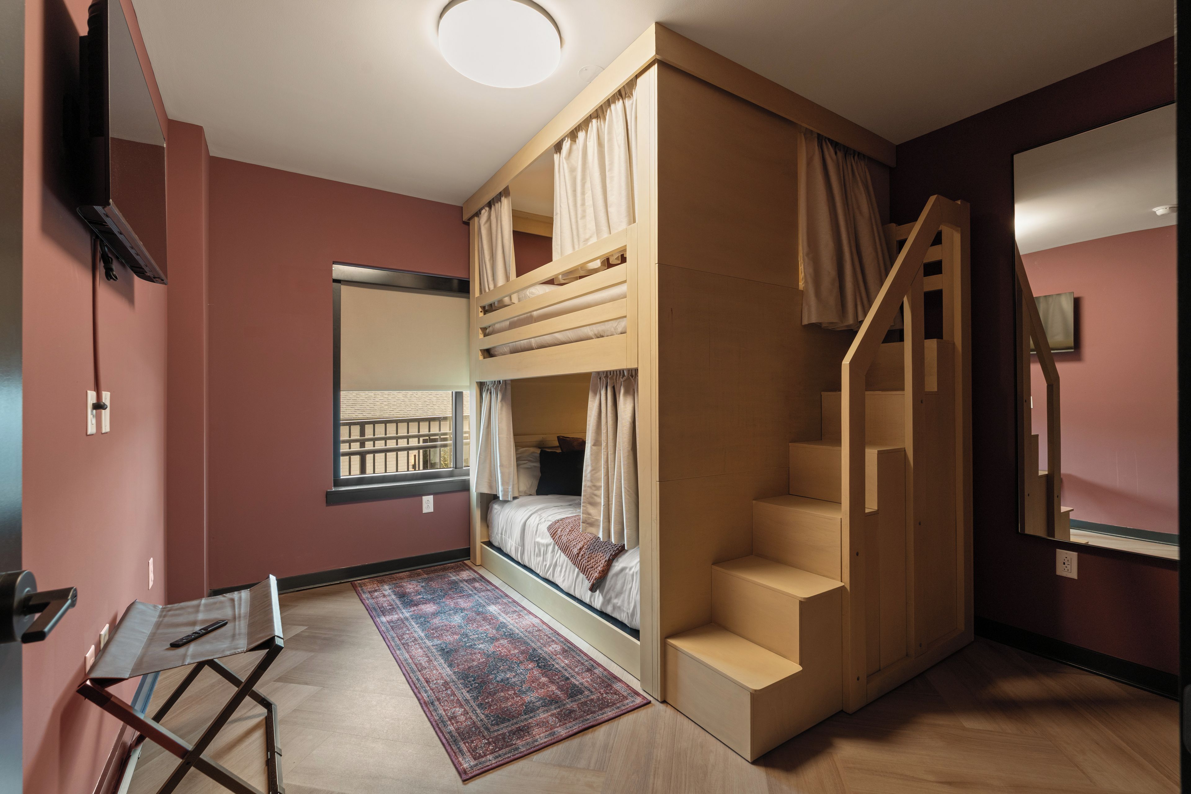 Una habitación con literas, un escritorio, una silla, una alfombra y una escalera.