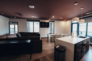 Eine moderne Küche mit einer zentralen Kochinsel, einem Essbereich mit Tisch und Stühlen sowie einem Wohnbereich mit Sofa und Fernseher.