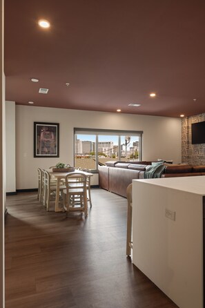 A modern living room with a sofa, a dining table with chairs, and a large window offering a city view. - Superior Suite - Unit 203 (Nashville)