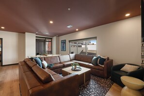 A modern living room with a sectional sofa, a coffee table, and a view of the cityscape through large windows. - Superior Suite - Unit 203 (Nashville)