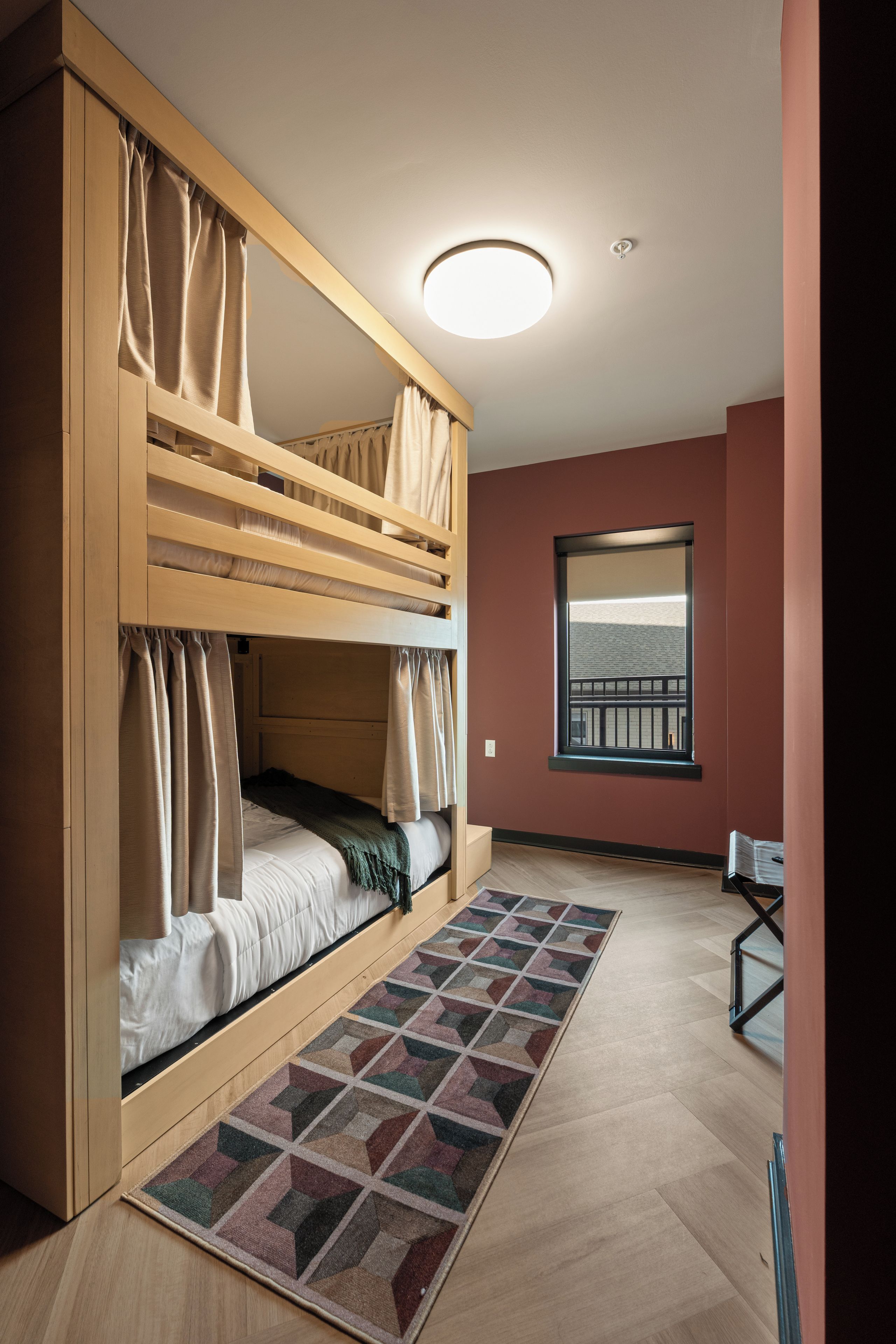 A bunk bed room with a window, a patterned rug, and a desk.