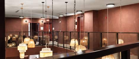Een hotelhal met meerdere hanglampen, een glazen balustrade en een zichtbaar vluchtsignaal.