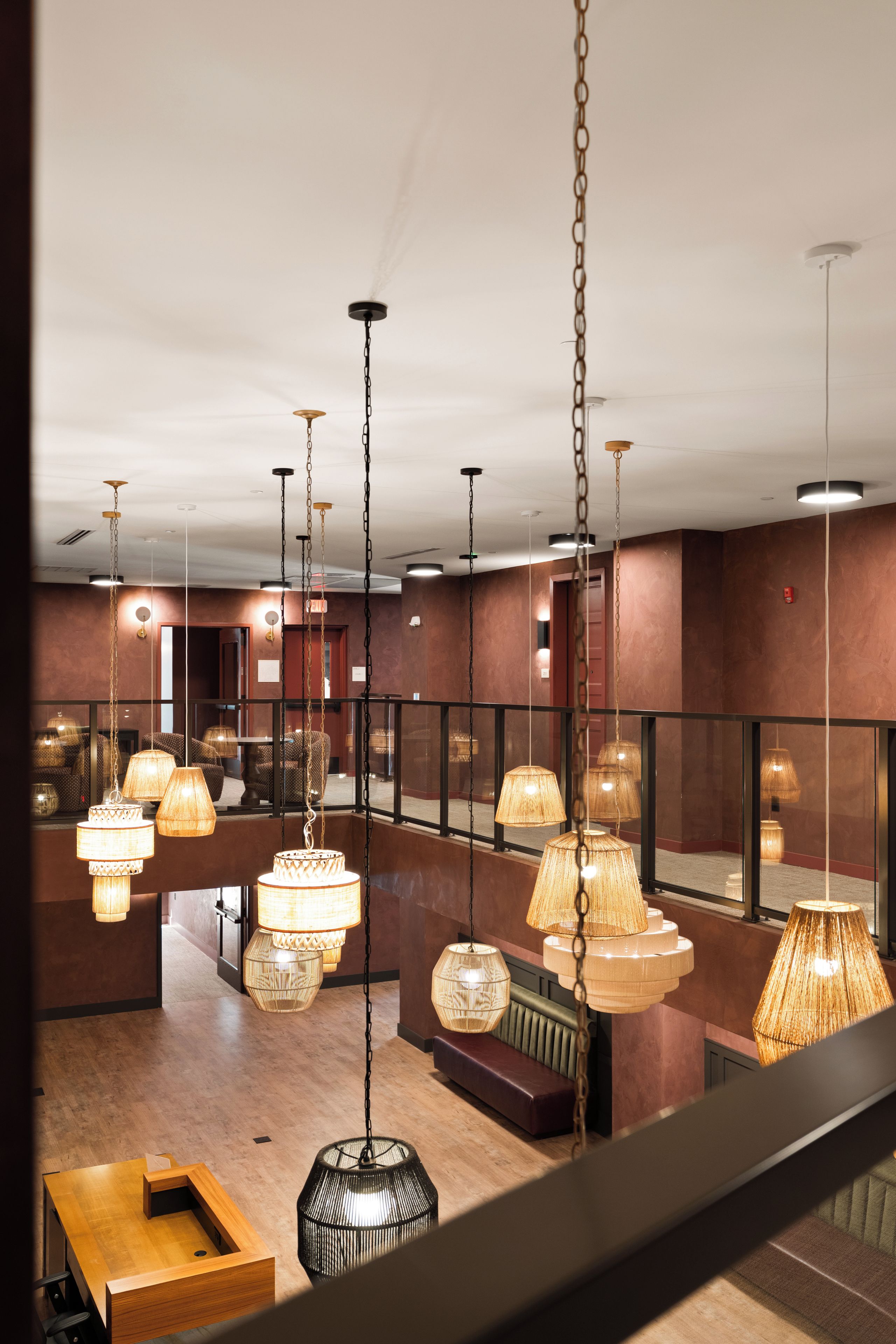 Un hall d’hôtel doté de plusieurs lampes suspendues, d’un comptoir d’accueil en bois et d’un espace salon.