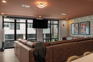 Un área de estar moderna con un sofá grande, un televisor de pantalla plana y amplias ventanas con vistas a la ciudad.