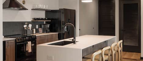 Une cuisine moderne dotée d’un îlot central, de tabourets de bar, d’une cuisinière en acier inoxydable et de luminaires suspendus.