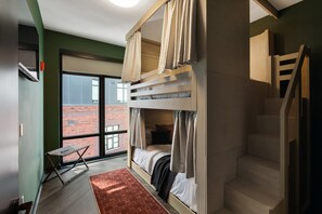 A room with a bunk bed, a small table, a chair, a window with a view of a brick building, and a staircase. - Superior Suite - Unit 301 (Nashville)