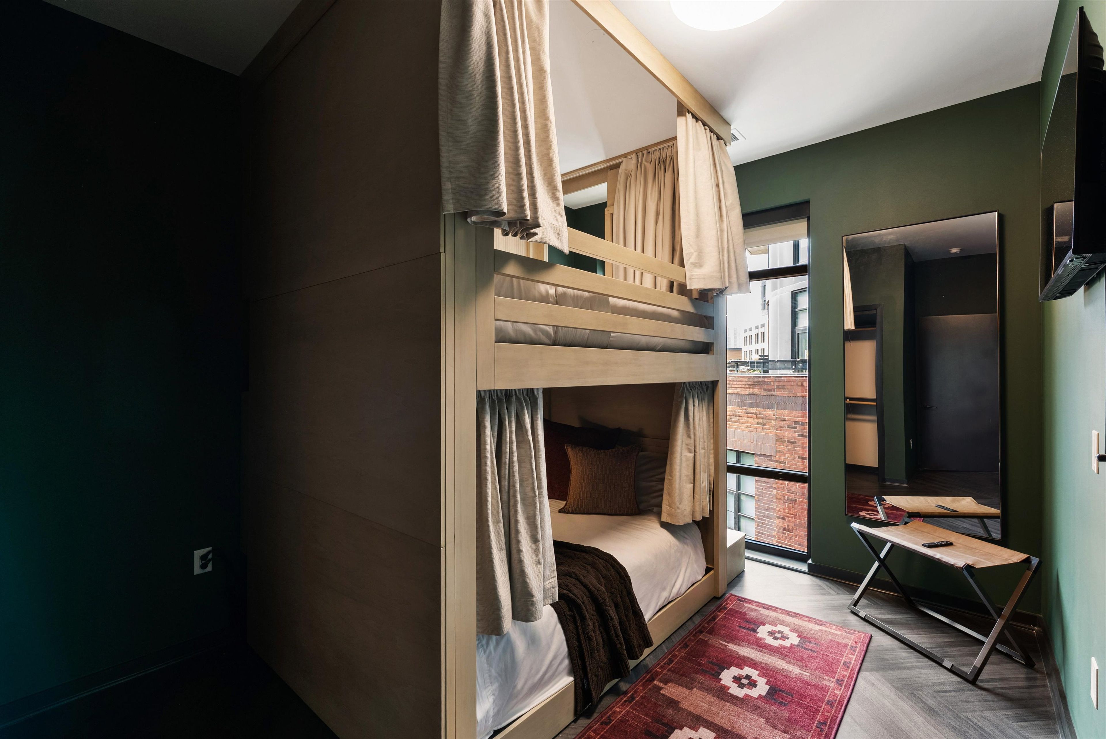 A compact room with a bunk bed, a small table, and a view of the outside.
