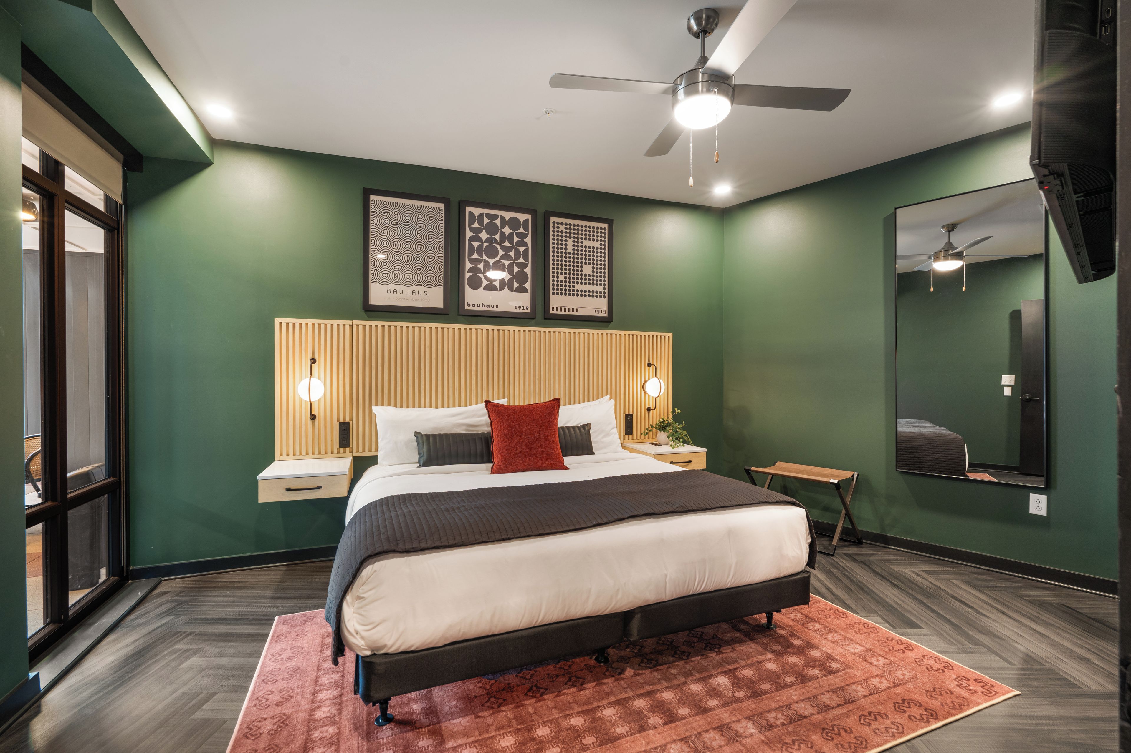 Une chambre à coucher moderne, avec un lit, des tables de chevet, un ventilateur de plafond et des œuvres d’art accrochées au mur.