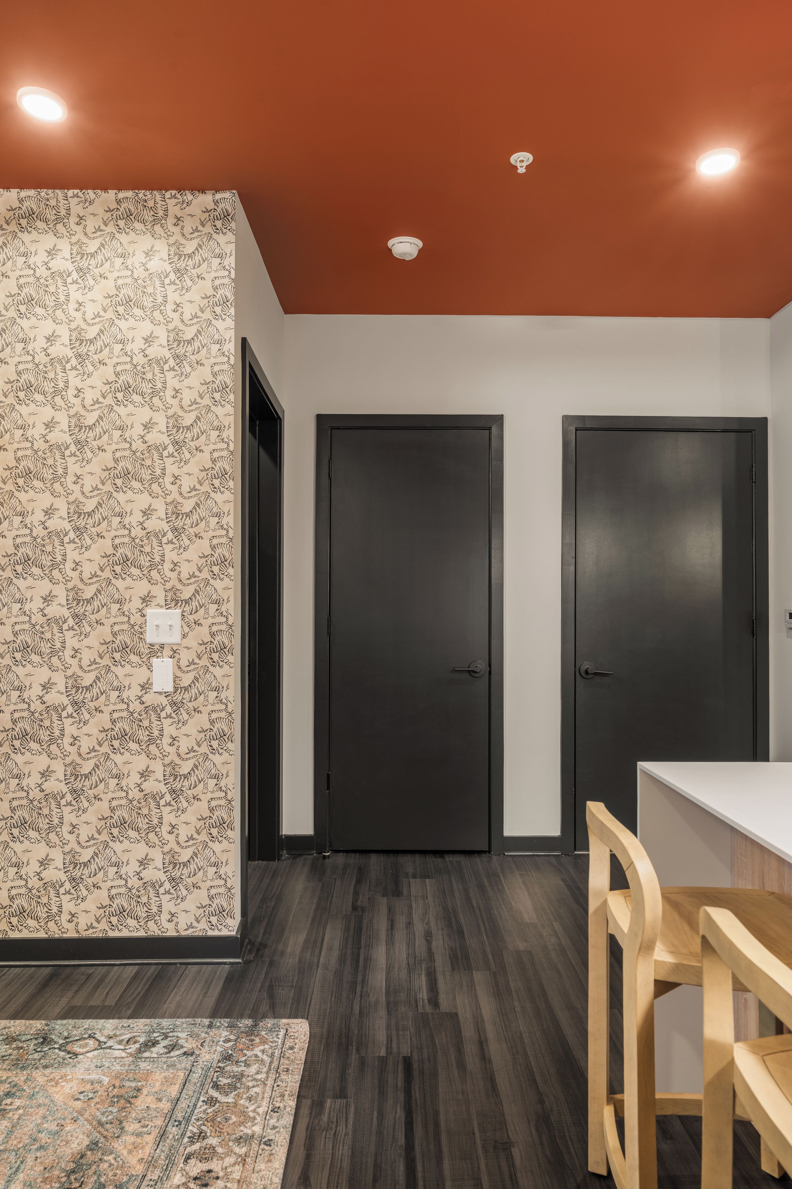 A room with a patterned wall, two dark doors, a white table, and a wooden chair.