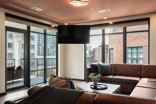 A modern living room with a large window, a flat-screen TV, and a leather sofa. - Superior Suite - Unit 401 (Nashville)