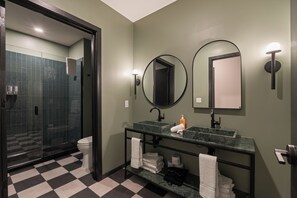 A bathroom with a checkered floor, two sinks, a glass shower enclosure, and a mirror with a round frame. - Superior Suite - Unit 401 (Nashville)