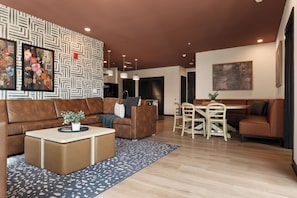 A modern living room with a brown leather sofa, a dining table with chairs, a coffee table with a plant, and a patterned wall. - Superior Suite - Unit 401 (Nashville)