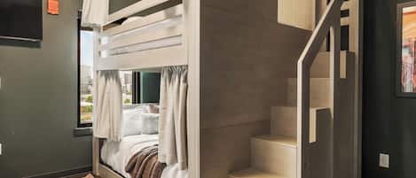 Habitación pequeña con una cama litera, una escalera y un ventanal grande.