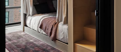 Un lit superposé avec des rideaux, un tapis à motifs et une vue sur un bâtiment en briques.