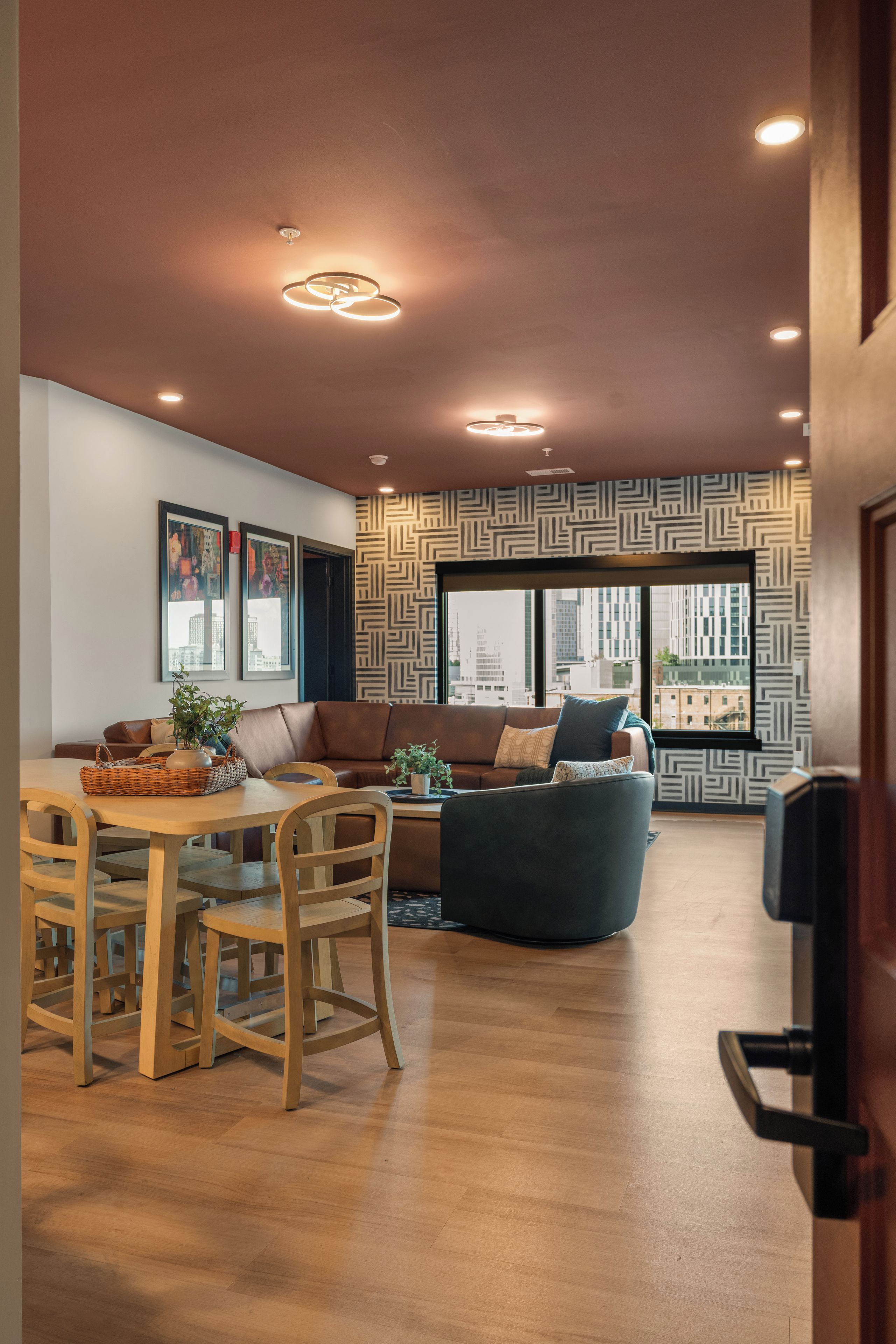 A modern living room with a brown leather sofa, a dining table with chairs, and a patterned wall.