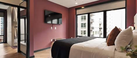 Une chambre moderne équipée d’un lit, d’un téléviseur à écran plat, d’un ventilateur de plafond et de grandes fenêtres.