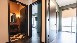 A hallway with a checkered floor, a mirror, a wall-mounted light, and a door leading to a balcony.