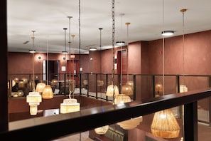 Eine Hotelhalle mit mehreren hängenden Lampen, einer Glasuhr und einem sichtbaren Hinweisschild für den Notausgang.