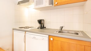 A compact kitchen with wooden cabinets, a built-in microwave, a coffee maker, and a dishwasher. - Cosy Alpine Studio With Wellness Access (Saint-Sorlin-d'Arves)
