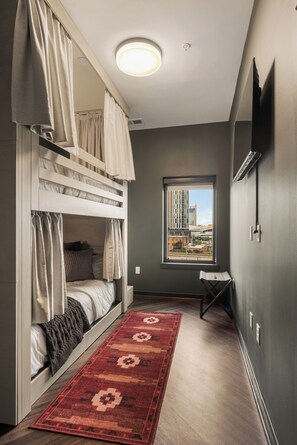A room with a bunk bed, a window with a city view, a red patterned rug, and a ceiling light. - Superior Suite - Unit 406 (Nashville)