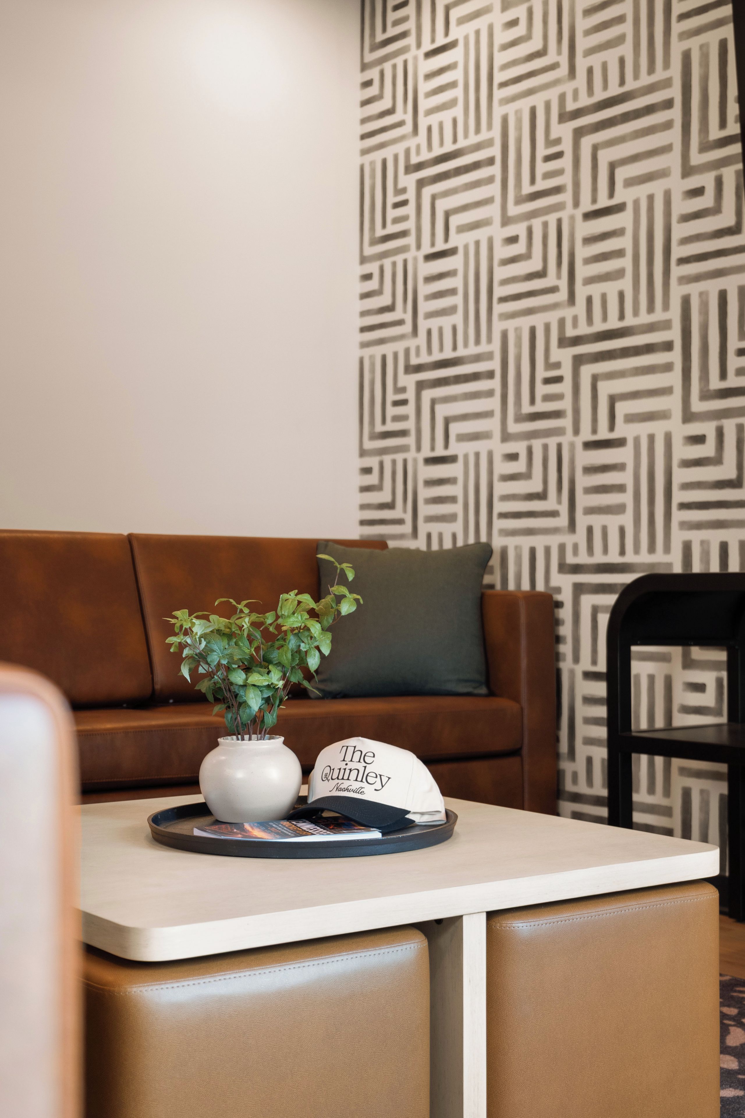 Uma sala de estar moderna com um sofá de couro marrom, uma mesa de centro branca com uma planta e uma placa, e uma parede com padrão.