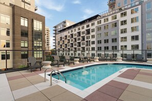Un hotel moderno con zona de piscina en la azotea, que incluye una piscina, sillas de descanso y vistas de los edificios circundantes.
