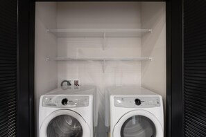 A laundry room with two white washing machines and two shelves above them. - Superior Suite - Unit 502 (Nashville)