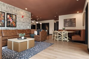 A modern living room with a brown leather sofa, a dining table with chairs, a coffee table with a plant, and a patterned wall. - Superior Suite - Unit 601 (Nashville)