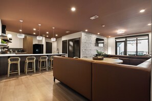 Cozinha moderna com ilha central, banquetas de bar e área de estar com sofá e almofadas.