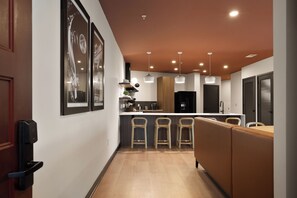 Uma cozinha moderna com ilha central, banquetas, luminárias pendentes e quadros nas paredes.