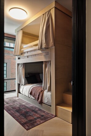 Un lit superposé avec des rideaux, un tapis à motifs et une vue sur un bâtiment en briques.