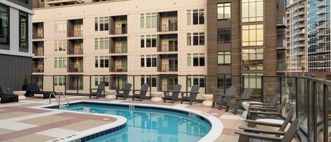 A modern building with multiple balconies and a swimming pool area with lounge chairs.