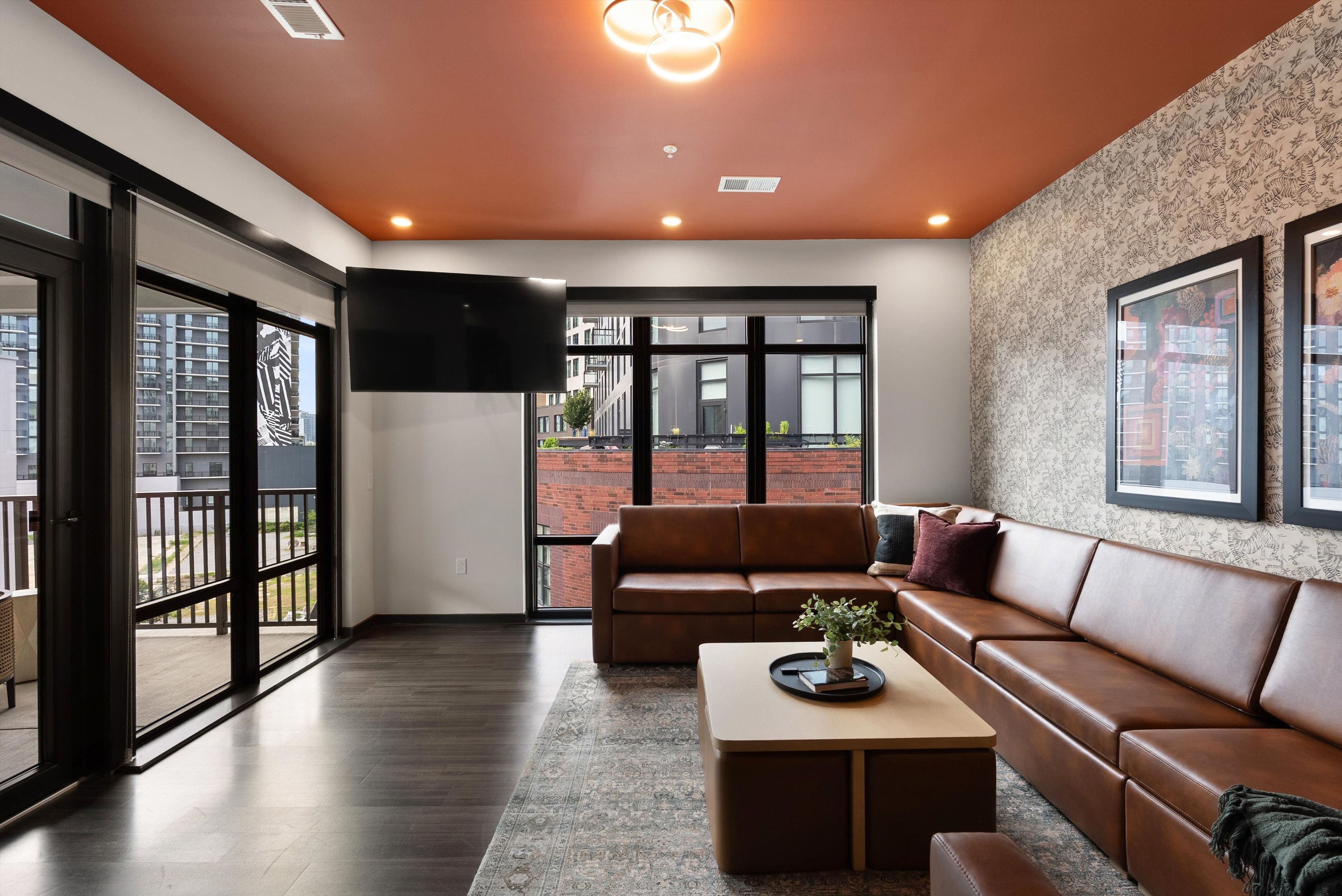A modern living room with a leather sofa, a coffee table with a plant, and a large TV mounted on the wall.