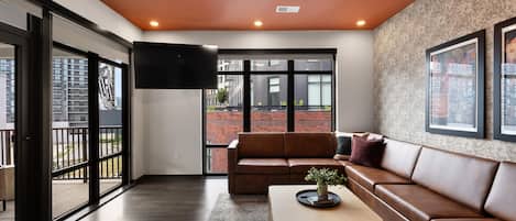 A modern living room with a leather sofa, a coffee table with a plant, and a large TV mounted on the wall.