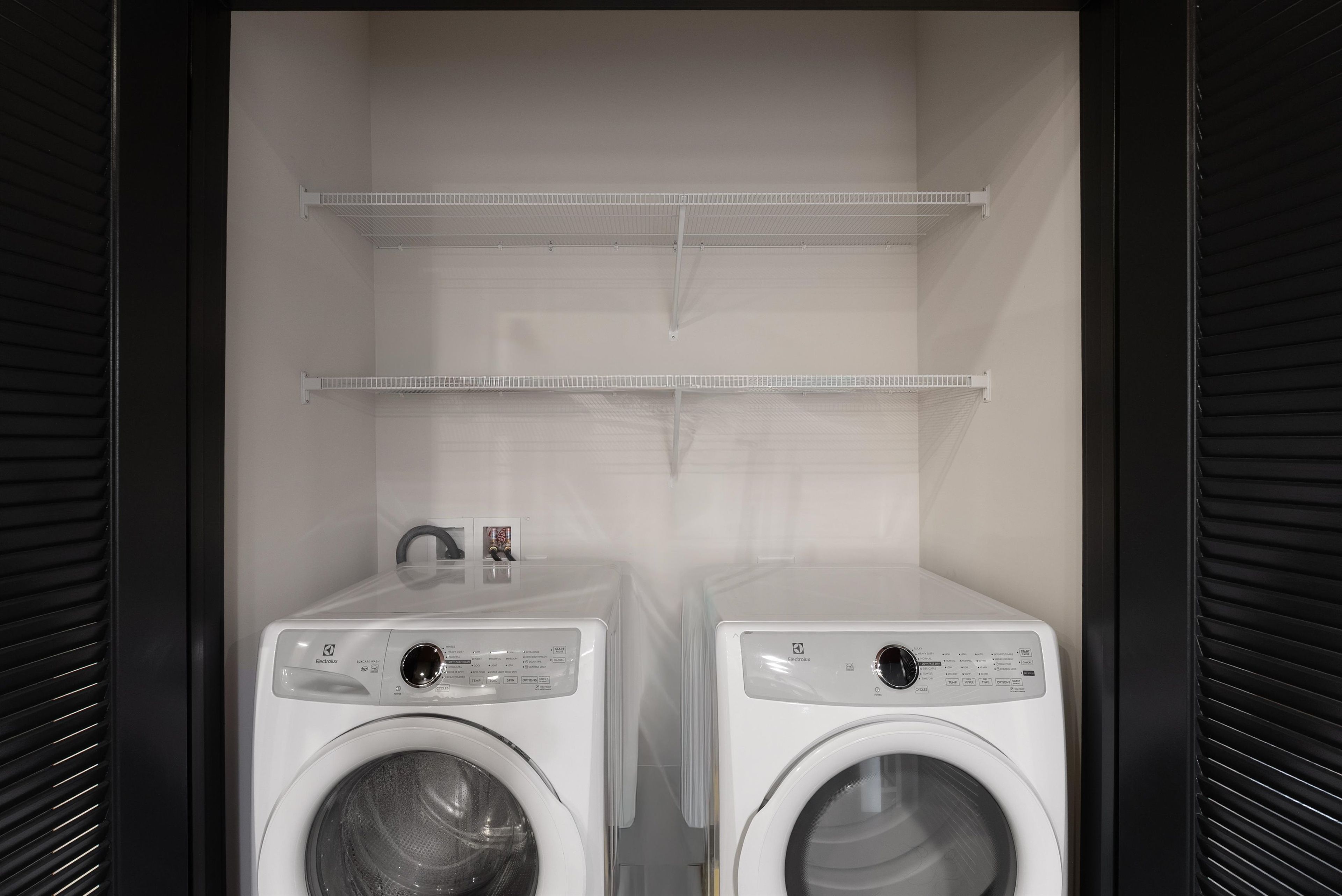 Une buanderie avec deux machines à laver blanches et deux étagères au-dessus.