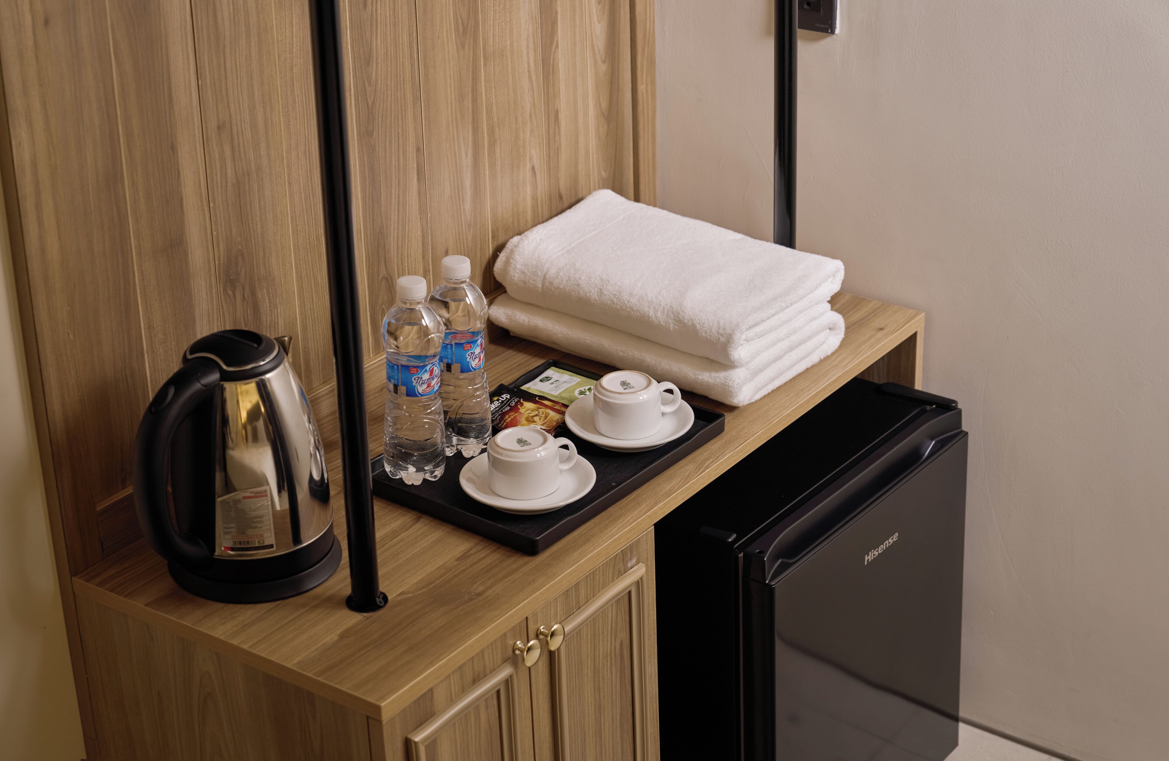 A minibar setup with a kettle, water bottles, tea bags, a tea set, and a folded towel.