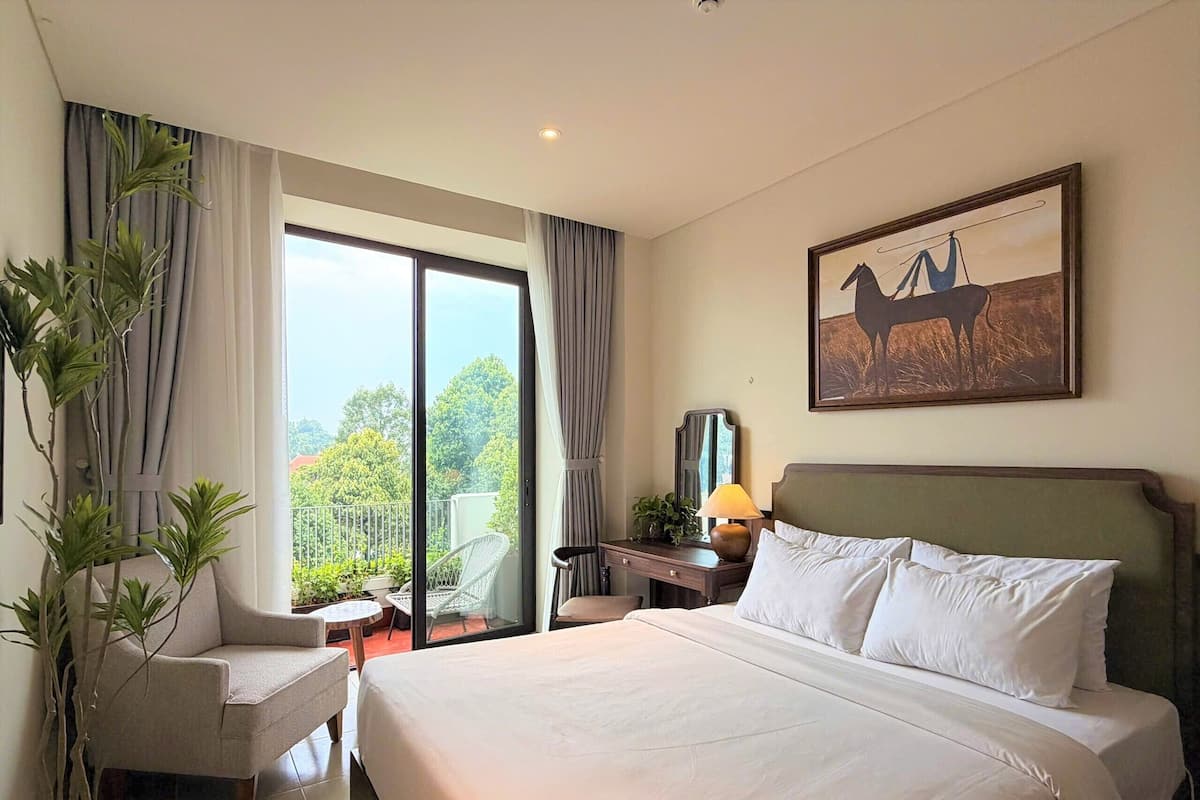 A hotel room with a large bed, a chair, a desk, a lamp, and a painting on the wall.