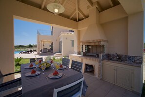 An outdoor dining area with a table set for two, a grill, and a view of the pool and landscape. - Stunning 4 Bed Villa, Sleeps 8 with breathraking views. Close to Katelios beach (Mavrata)