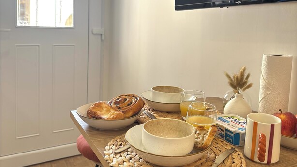 Une table de petit-déjeuner avec du pain, un muffin, un verre de jus de fruits et une tasse.
