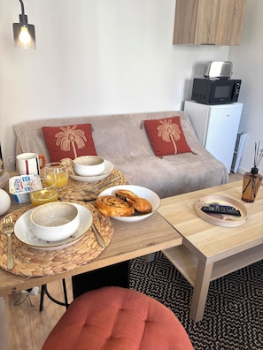 Un espacio de sala acogedor con un sofá, una mesa de centro y una mesa de comedor con alimentos para el desayuno.