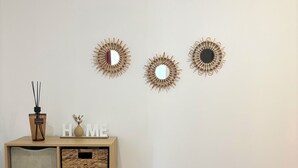 Une pièce comprenant un meuble en bois, des paniers en osier, un pouf rond en osier et trois miroirs décoratifs fixés au mur.