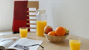 En frukostuppdukning med ett bord, en stol, en korg med frukt, en kanna med apelsinjuice och ett glas juice.