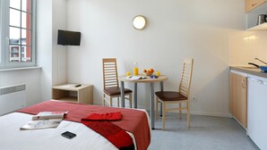 Ett hotellrum med en säng, ett litet bord med frukosttillbehör, två stolar, en TV och ett litet pentry.