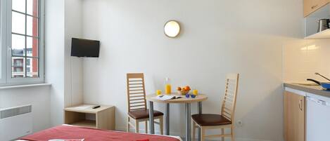A hotel room with a bed, a small table with breakfast items, two chairs, a TV, and a kitchenette.