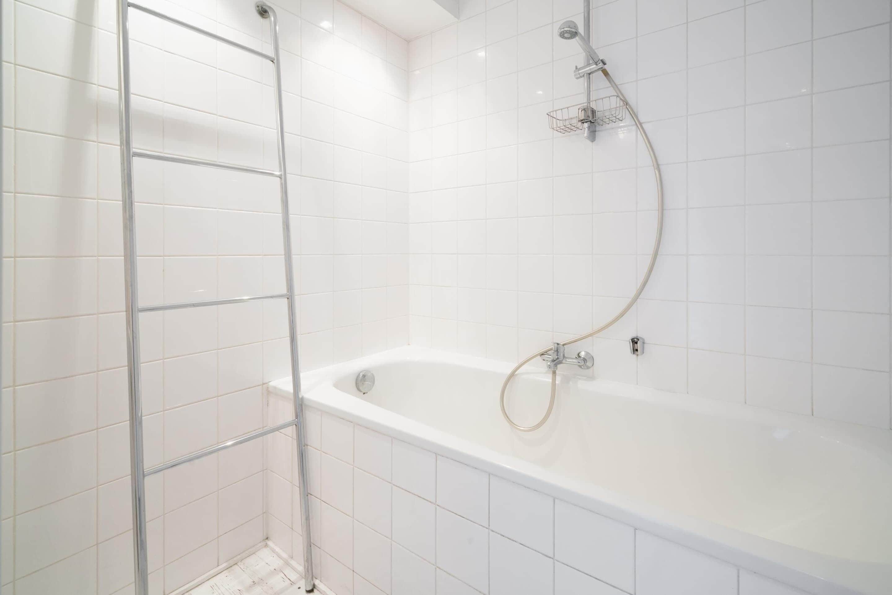 A modern bathroom with white tiles, a freestanding bathtub, and a shower with a handheld hose.