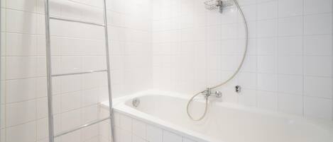 A modern bathroom with white tiles, a freestanding bathtub, and a shower with a handheld hose.