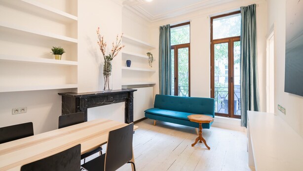 A modern living room with a sofa, a dining table, chairs, a small round table, and a fireplace. - 1-bedroom Apartment in National Residence (Antwerp)