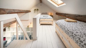 A loft bedroom with a skylight, wooden beams, a bed with patterned bedding, a bench, and a small seating area. - 1-bedroom Apartment in National Residence (Antwerp)